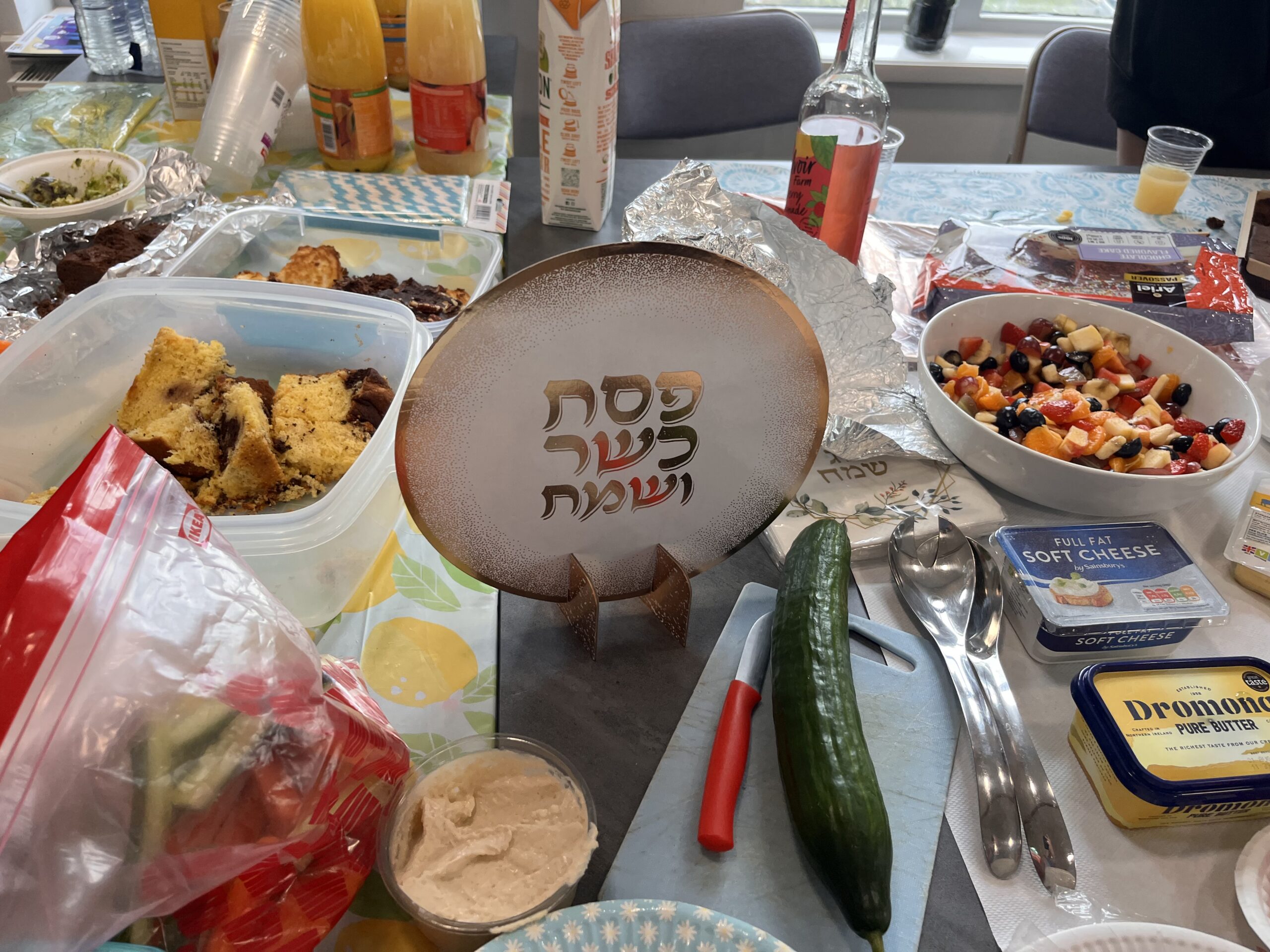 Close up of a table with many types of food and a decorated plate in the centre reading "Chag Peach Sameach" in Hebrew.